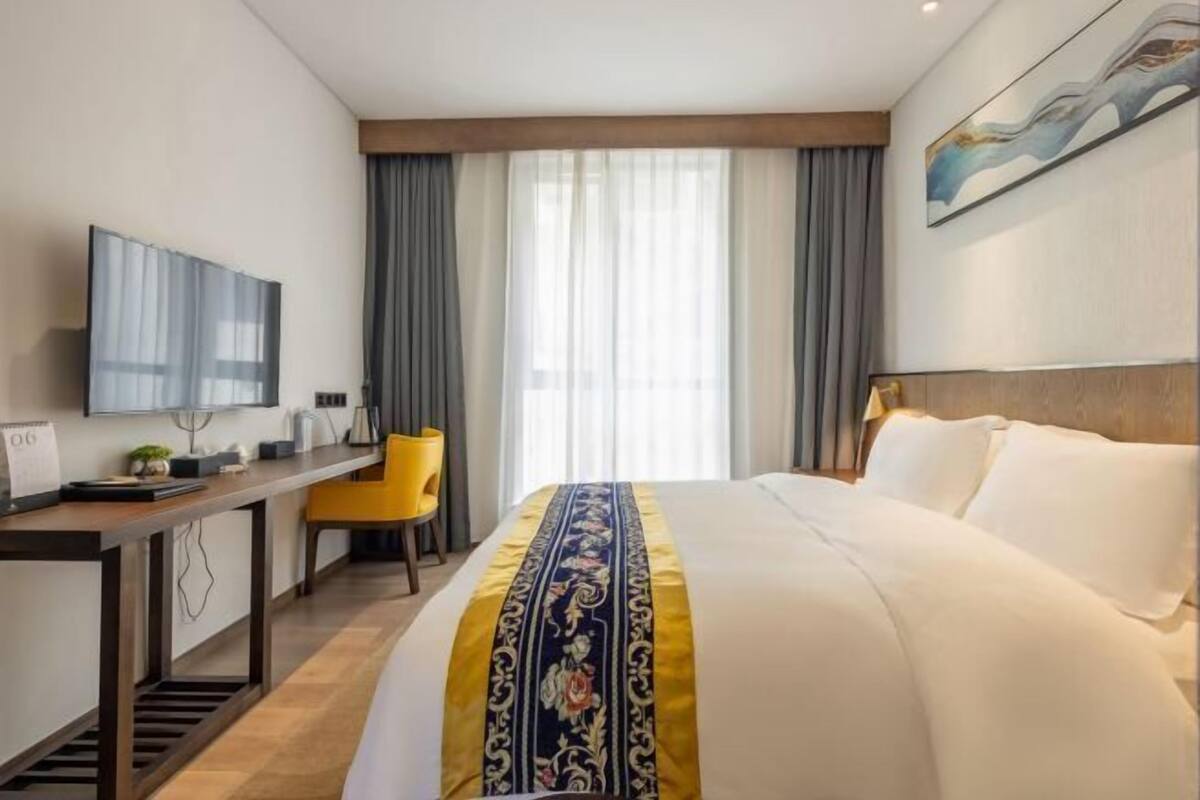 A hotel room with a bed, a desk, a chair, a TV, and a window with curtains.