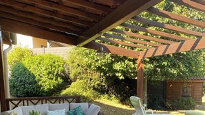 Uma área de estar coberta ao ar livre, com móveis de vime e uma pérgola de madeira.