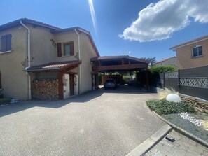 En uppfart som leder till ett bostadshus med ett takbeklätt carport och en hög med ved.