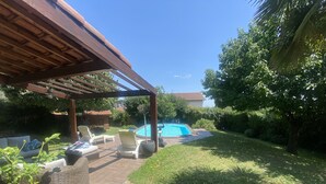 Uma área de varanda coberta com cadeiras de descanso, uma piscina pequena e um gramado bem cuidado.