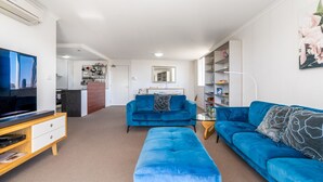 En moderne stue med en blå sofa, et matchende fodskammel og et fladskærms TV på et træstel.