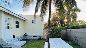 En trädgård med ett picknickbord, en möblerad uteplats under tak och ett hus med en dörr och fönster.