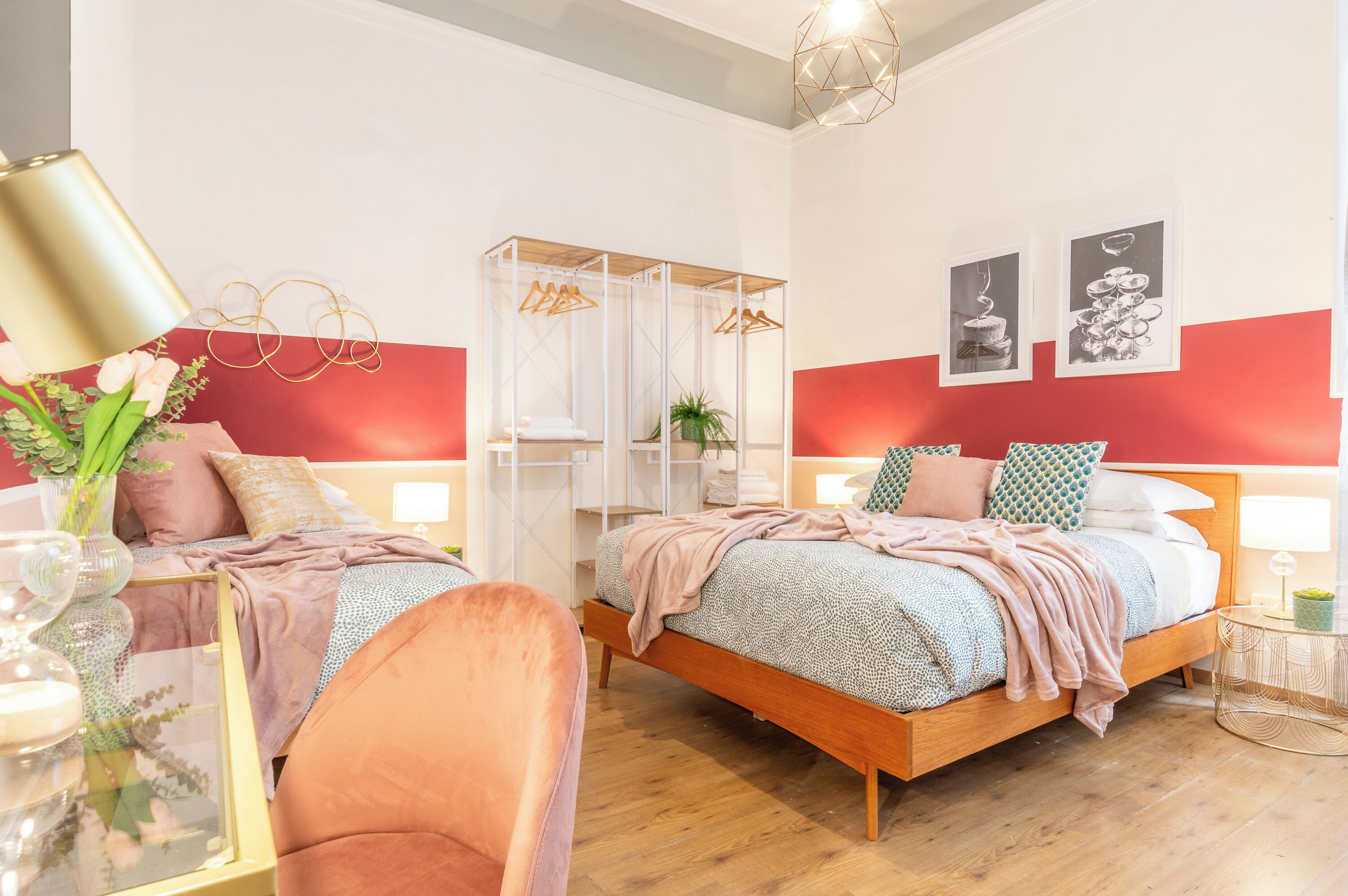 Un dormitorio moderno con una cama de madera, una mesita de vidrio con un florero, una silla rosa y un armario blanco.