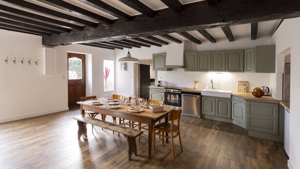 A dining area with a wooden table set for four, a bench, and a kitchen with green cabinets and modern appliances. - Offrez-vous des Vacances Dans un Grand Domaine Privé Rien que Pour Vous! (Archignat)