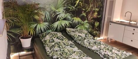 A room with a bed, a white cabinet, and a wall mural of tropical foliage.