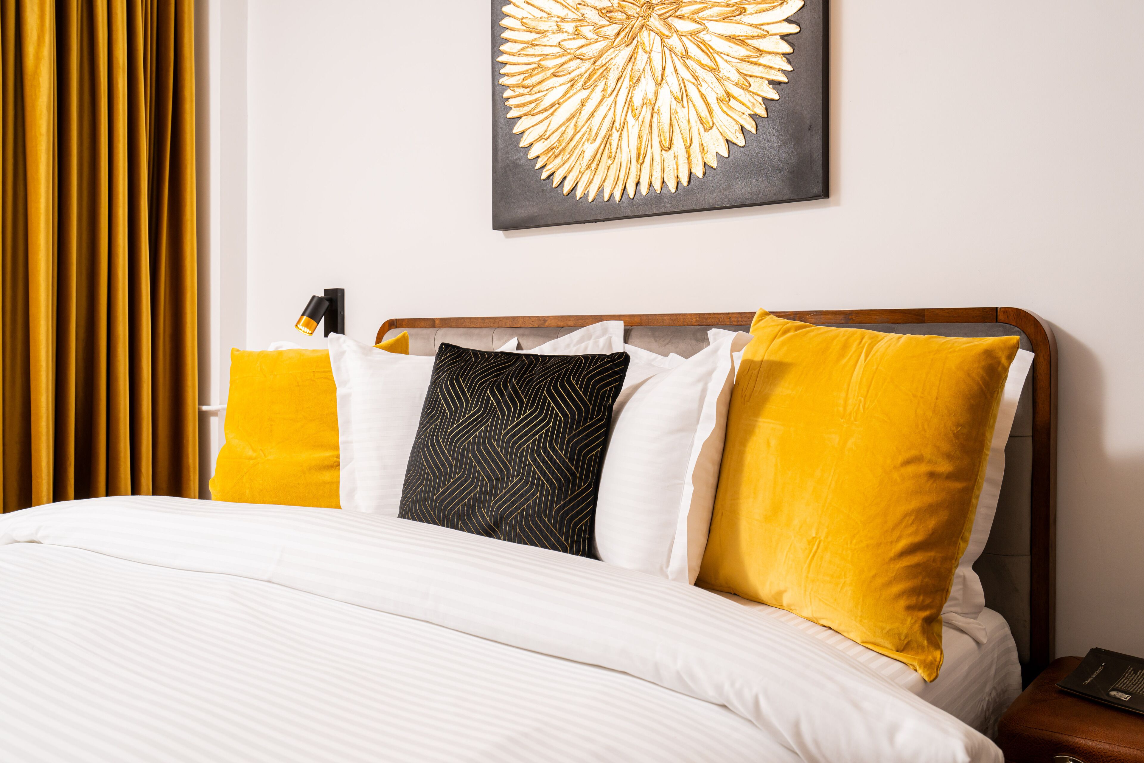 A neatly made bed with white linens and multiple pillows, including yellow and patterned ones.