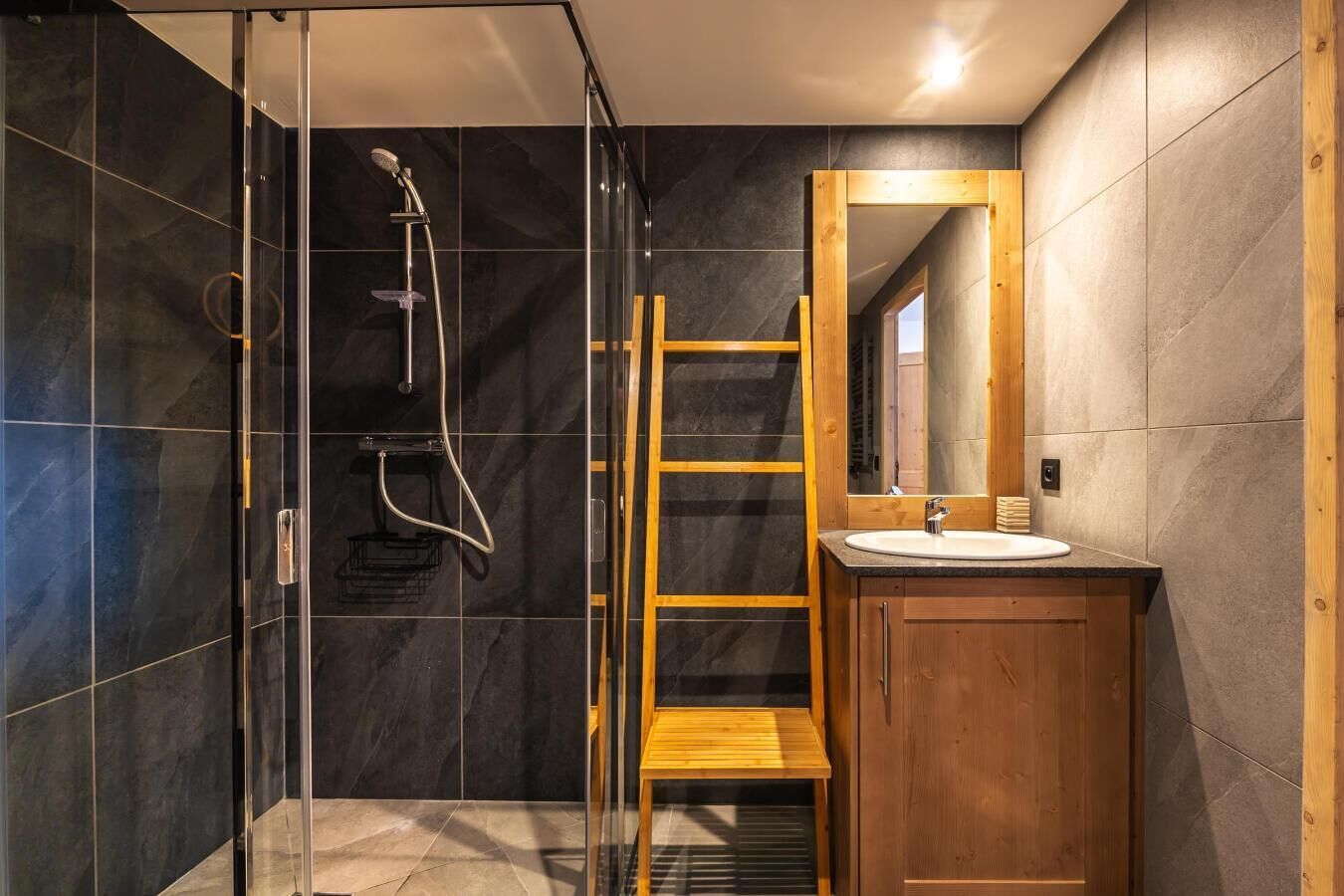 Une salle de bain moderne avec une douche à parois de verre, une échelle en bois et un meuble-lavabo en bois avec un miroir.