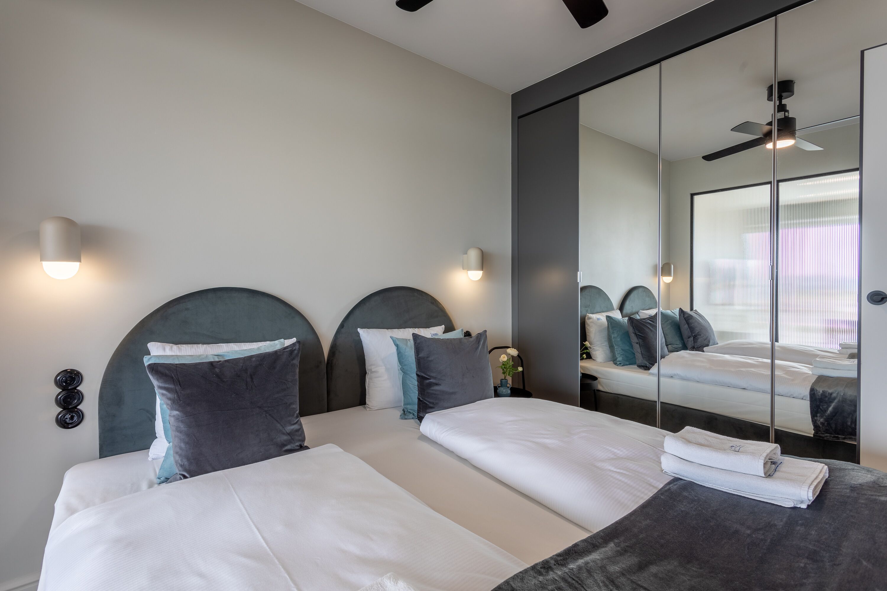 Una camera d'albergo moderna con un letto grande, due comodini, uno specchio e una ventola a soffitto.