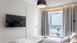 Une chambre d’hôtel moderne, équipée d’un lit, d’un téléviseur fixé au mur et offrant une vue sur la ville par la fenêtre.