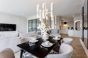 Een moderne eetruimte met een zwarte tafel gedekt voor vier personen, omringd door grijs gestoffeerde stoelen. Op tafel staat een witte vaas met bloemen, en er is een groot raam op de achtergrond.