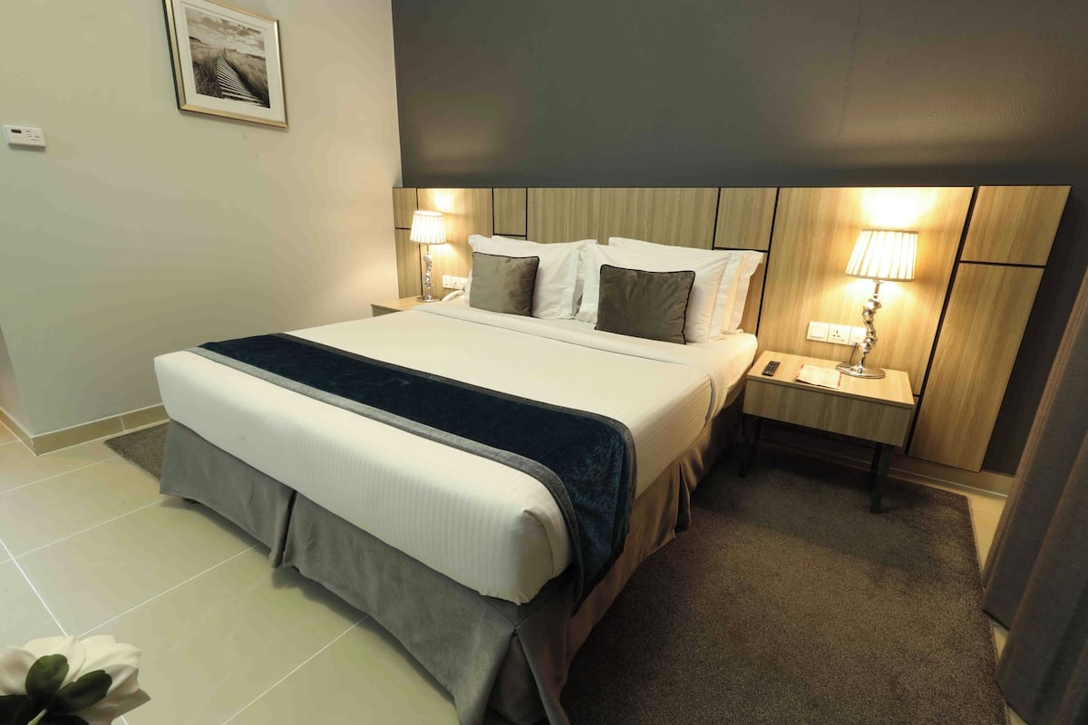 A neatly made bed with a dark headboard, a bedside table with a lamp, and a framed picture on the wall.
