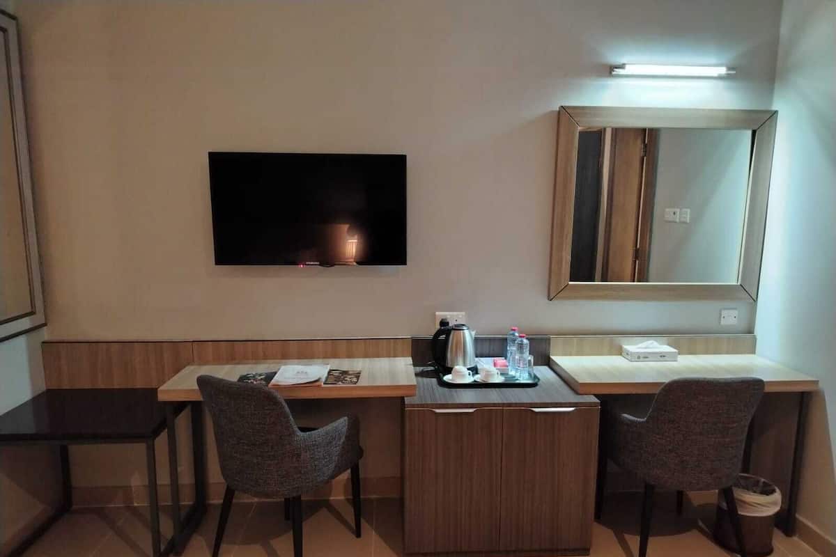 A hotel room with a wooden desk, two chairs, a flat-screen TV, a coffee maker, and a mirror.