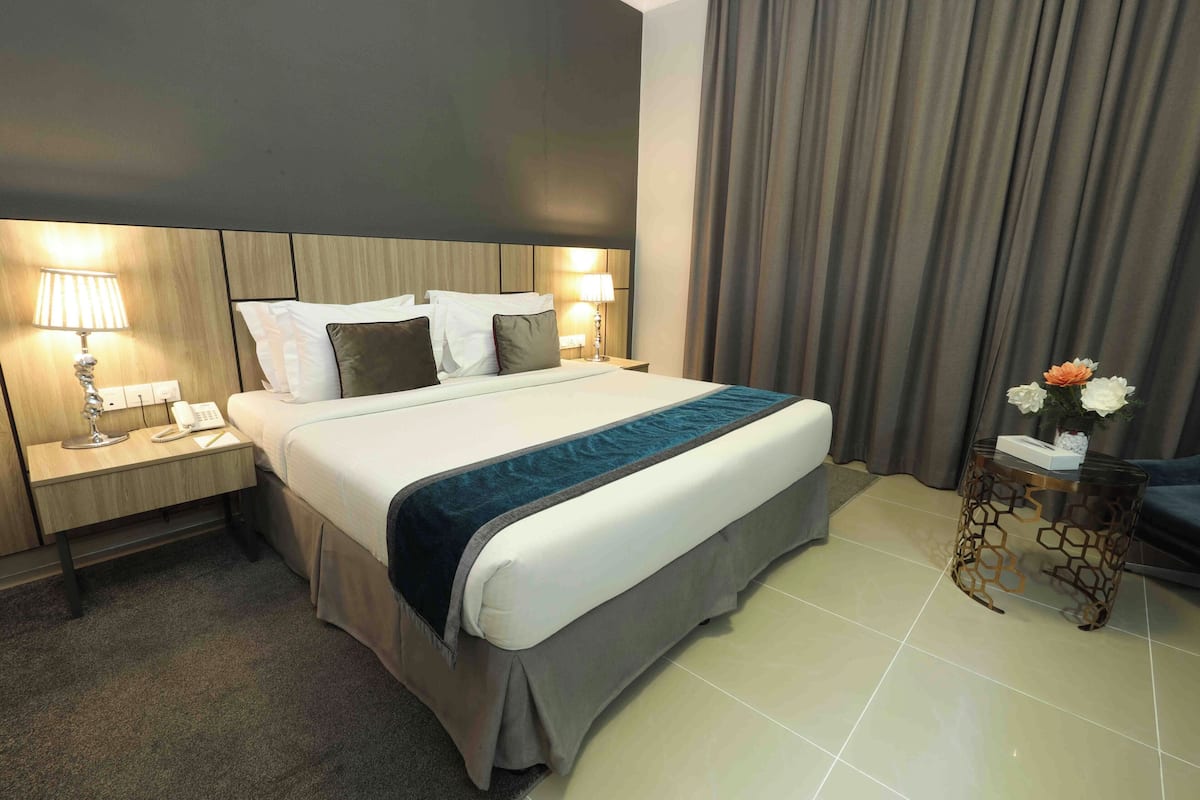 A hotel room with a large bed, bedside lamps, a small table with a vase of flowers, and a curtain.