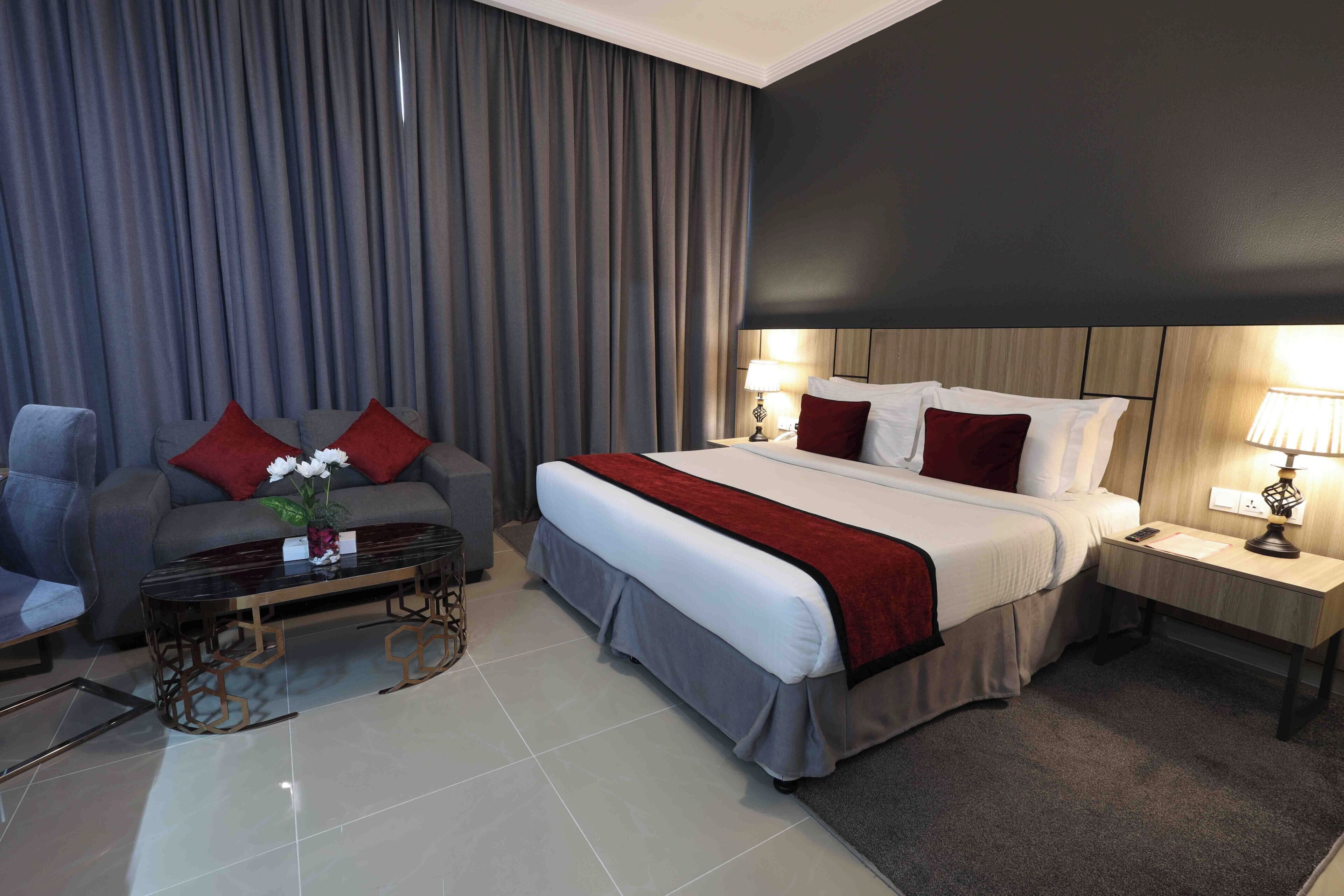 A hotel room with a bed, a sofa, a coffee table, and a nightstand with lamps.