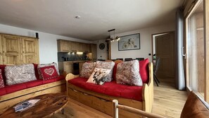 Ein gemütliches Wohnzimmer mit einem roten Sofa, Holzschränken, einem Essbereich und einer Küche im Hintergrund.