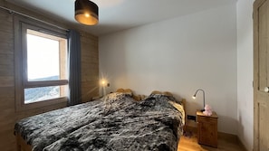 Ein Schlafzimmer mit einem Bett, einem Nachttisch, einer Lampe und einem Fenster mit Vorhängen.