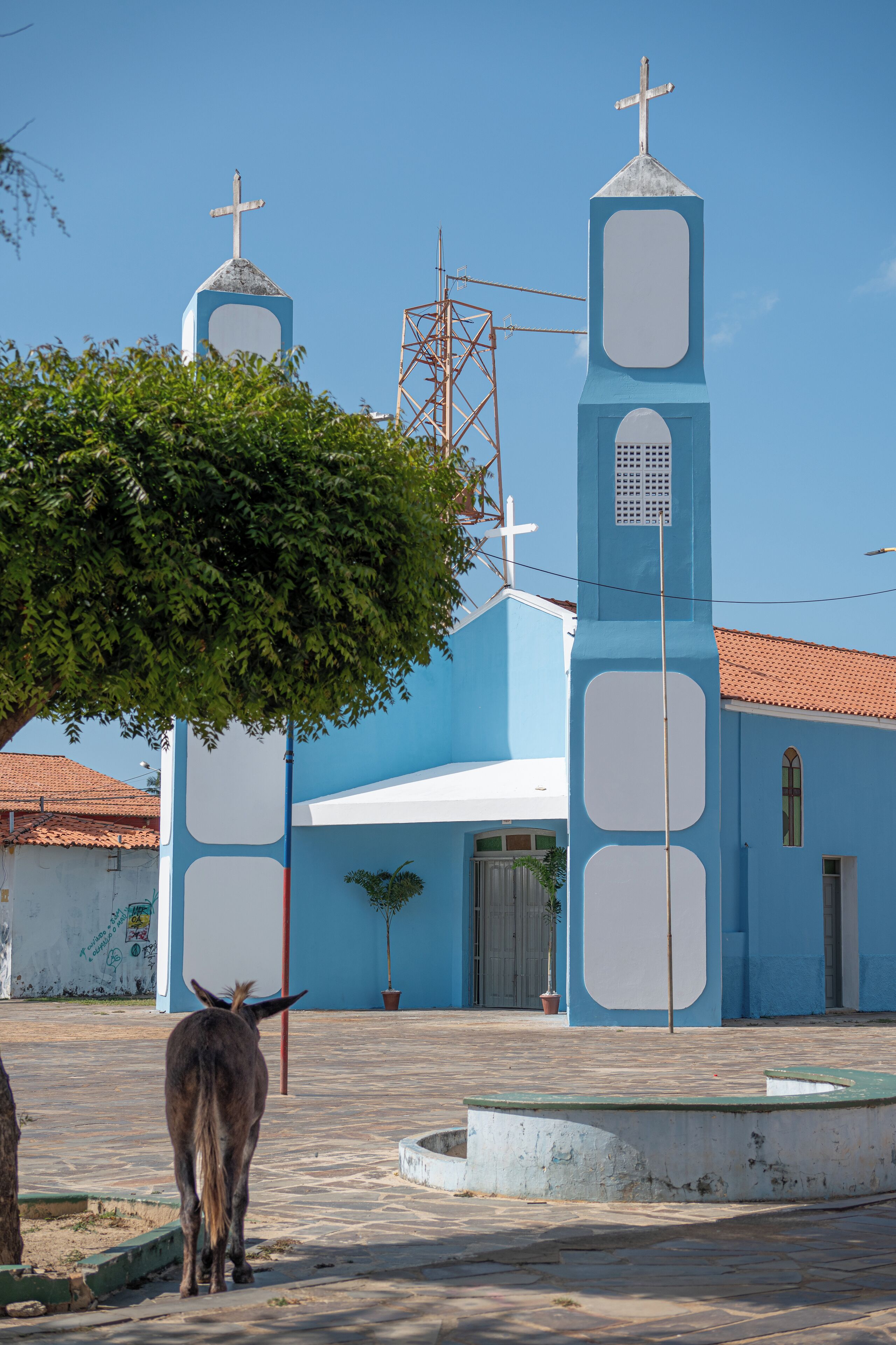 Igreja com fachada azul, uma torre sineira e uma cruz no topo.