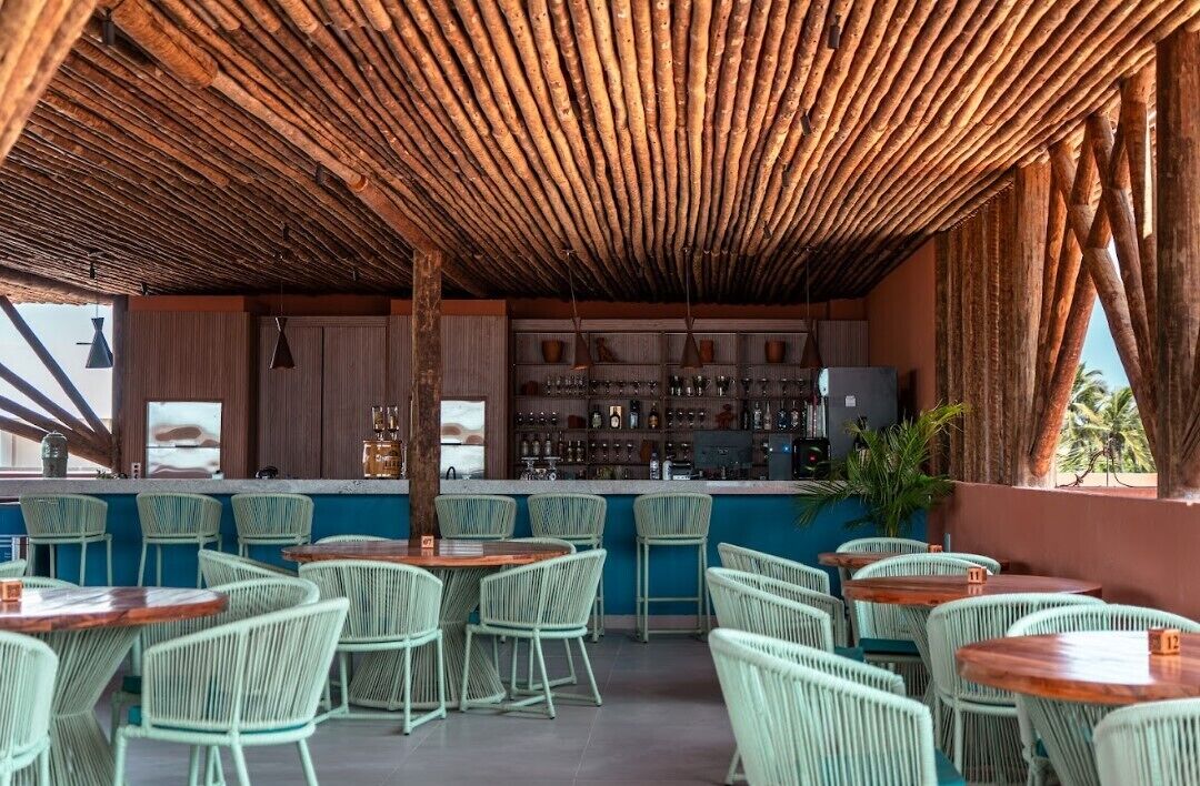 An outdoor bar area with wicker chairs and tables, a wooden ceiling, and a bar counter with various bottles and glasses.