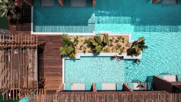 An aerial view of a pool area with wooden deck seating and palm plants.