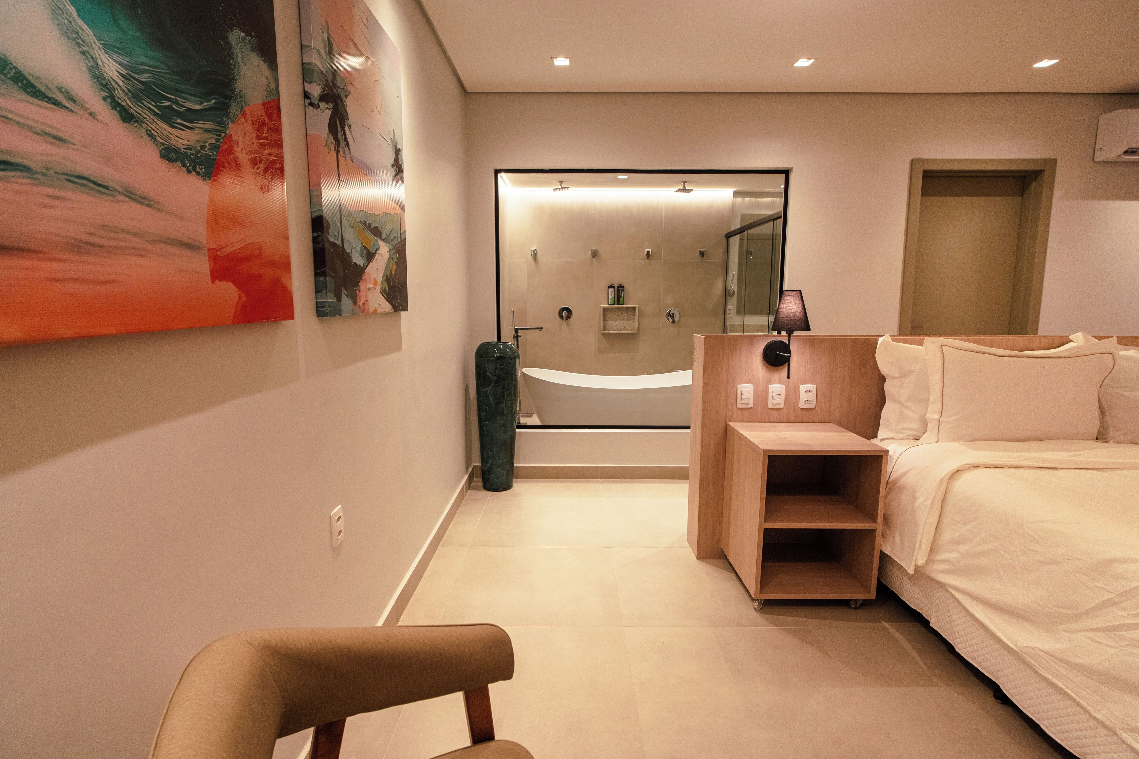 Ein modernes Hotelzimmer mit einem großen Bett, einem Nachttisch, einem Sessel, einer Duschkabine und Bildern an der Wand.