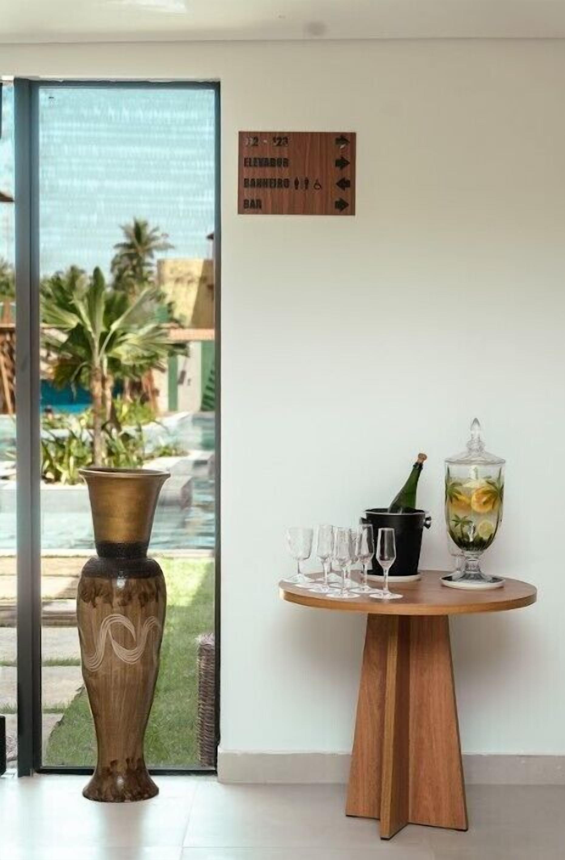 Une pièce avec une table en bois dressée pour un repas, un vase et une vue sur une piscine et des palmiers à l’extérieur.