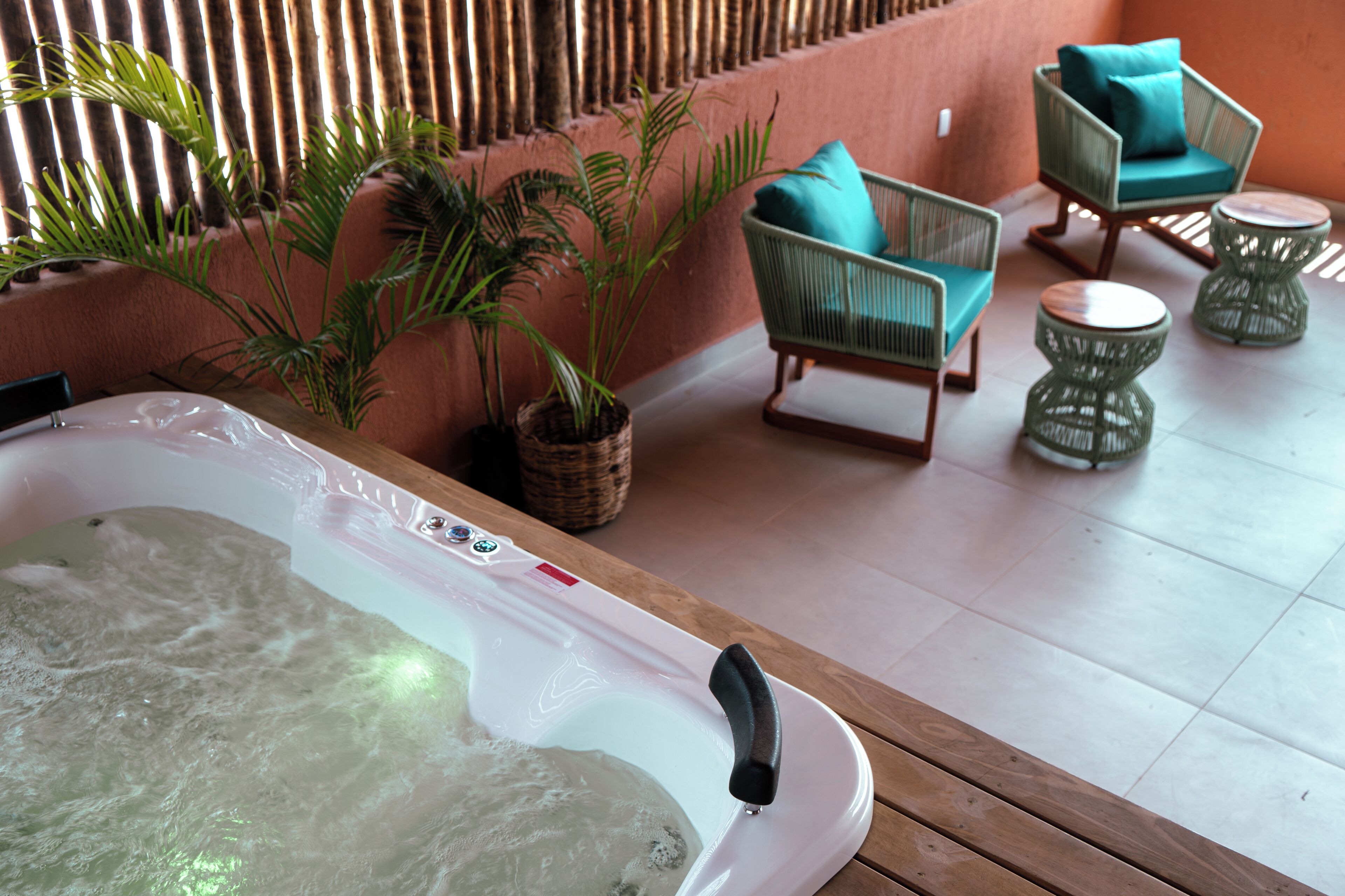 Un espace bien-être comprenant un jacuzzi, des fauteuils en osier et des plantes en pot.