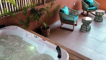 Un espace bien-être comprenant un jacuzzi, des fauteuils en osier et des plantes en pot.