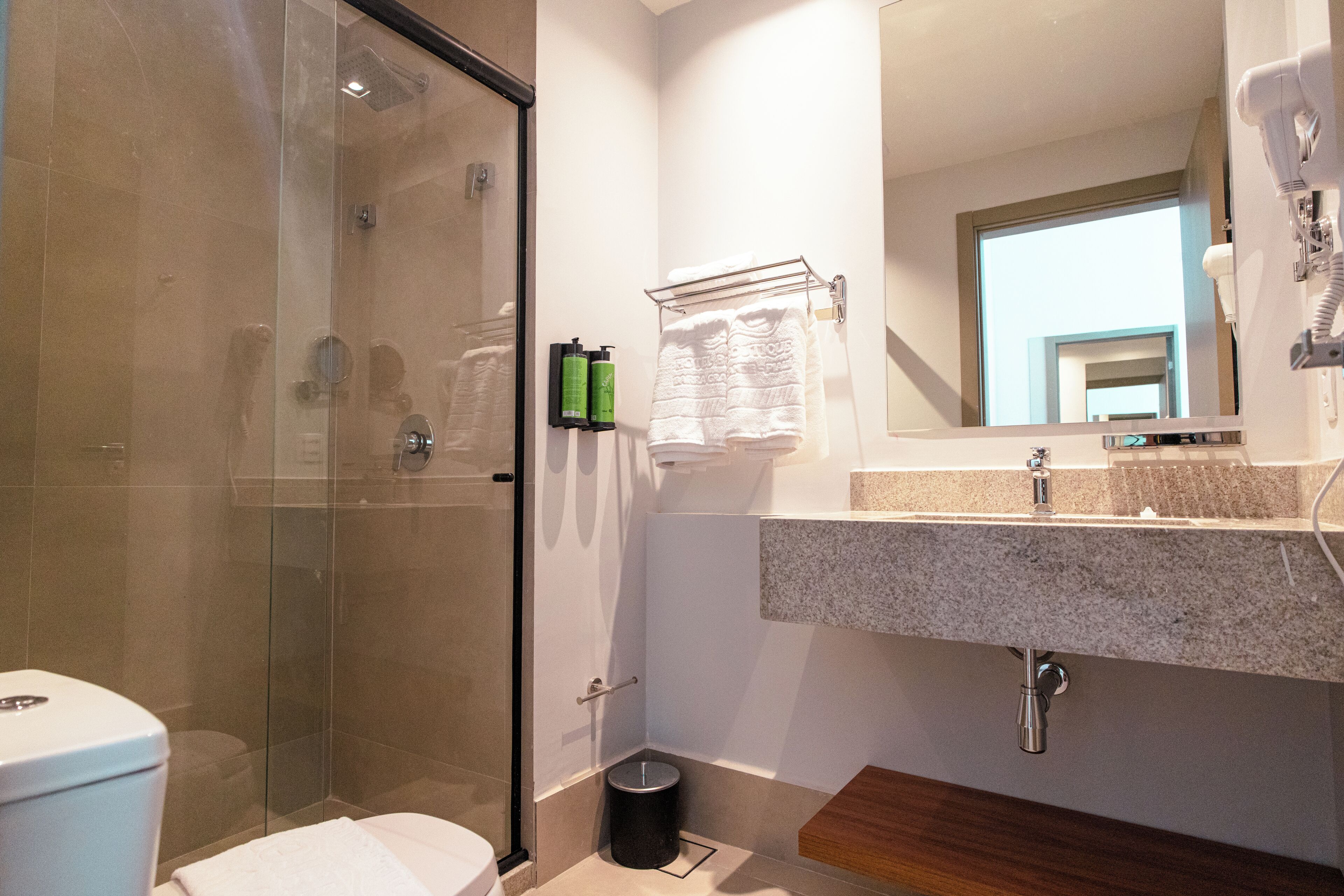 A modern bathroom with a glass shower enclosure, a white toilet, a sink with a granite countertop, and a mirror above the sink.