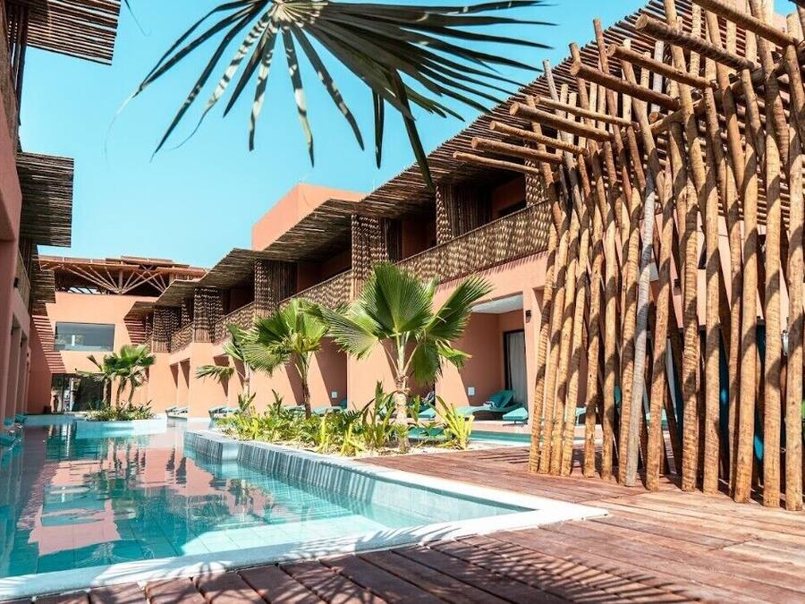 Un área de piscina con terraza de madera, palmeras y cielo azul.