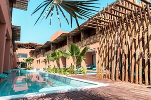 Área de piscina com deck de madeira, palmeiras e céu azul límpido.