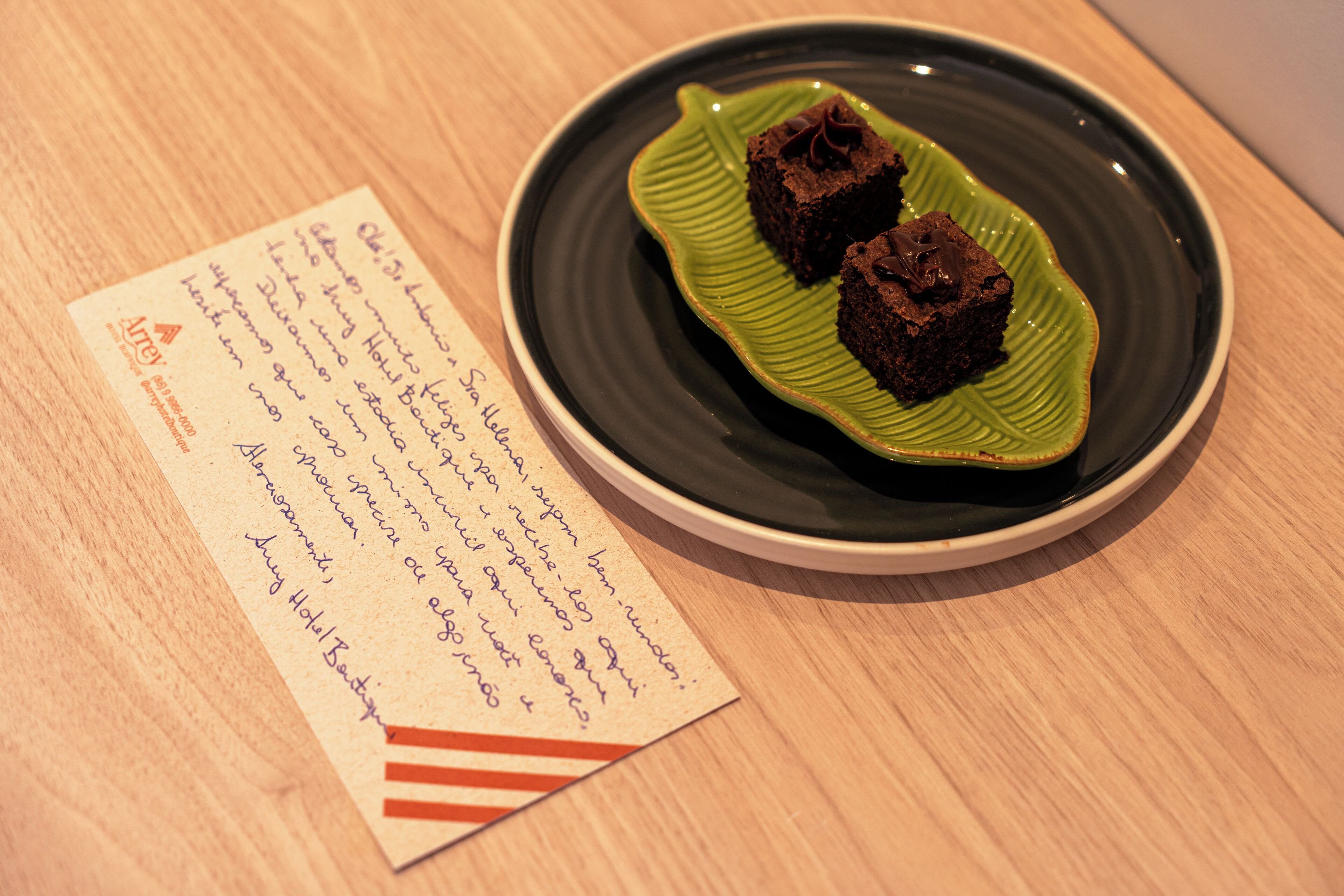Un plato con dos brownies sobre una hoja verde modelada en cerámica, junto a una nota escrita a mano.