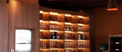 Un espace bar avec des étagères remplies de bouteilles et de verres, un mur recouvert de panneaux en bois et des luminaires suspendus.