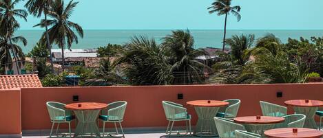 Terraço com área de estar ao ar livre, com vista para a costa, palmeiras e o mar.