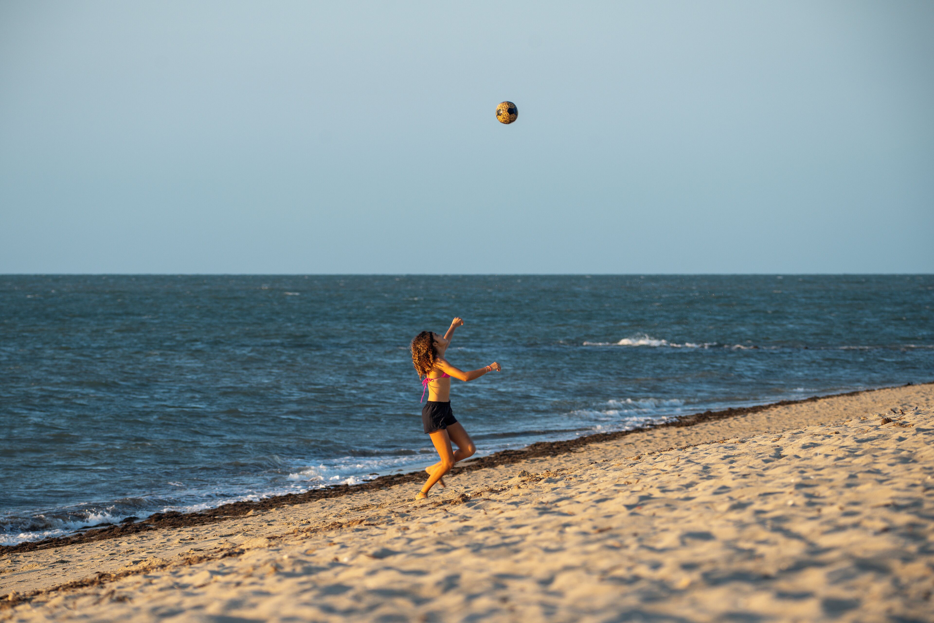 A person playing with a ball on a sandy beach with the ocean in the background.