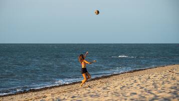 A person playing with a ball on a sandy beach with the ocean in the background.