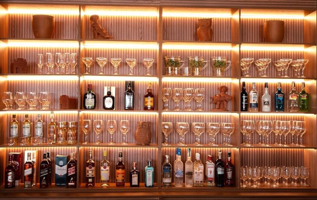 Un bar avec des étagères remplies de bouteilles d’alcool et de verres de toutes sortes.