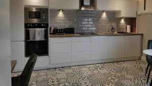 A modern kitchen with a built-in oven, microwave, and stove, white cabinets, and a patterned tile floor. - Seaview Terrace (Skerries)