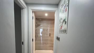 Un couloir avec un espace douche, une affiche accrochée au mur et une porte donnant sur une autre pièce.