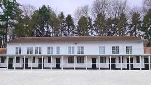 A white building with multiple windows and a tiled roof, surrounded by trees. - Royal Horses (Overijse)