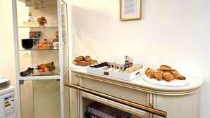 A kitchenette with a white cabinet containing various food items, a small refrigerator, and a countertop with pastries and a coffee machine. - Royal Horses (Overijse)