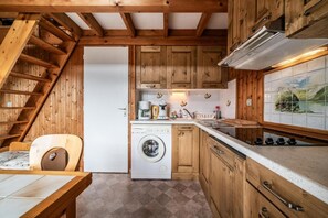 A compact kitchen with wooden cabinets, a built-in washing machine, and a dining area with a table and chairs. - Chalet, wifi, Ground floor, view mountain, parking, tv, 53m², Les Gets (Les Gets)
