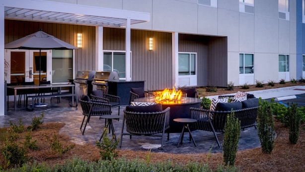 An outdoor patio area with a fire pit, seating, and a grill. - Towneplace Suites by Marriott Brunswick (Brunswick)