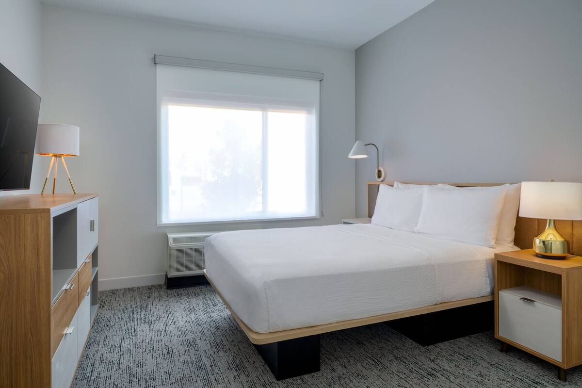 Ein Hotelzimmer mit einem Bett, Nachttischen, einem Fernseher und einem Fenster mit Jalousien.