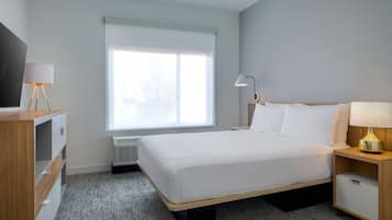 A hotel room with a bed, bedside tables, a TV, and a window with blinds.