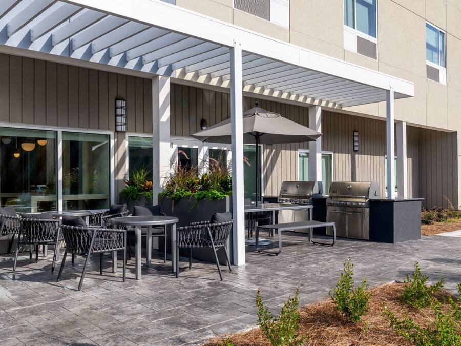 An outdoor patio with tables and chairs, a grill, and a covered area with plants.