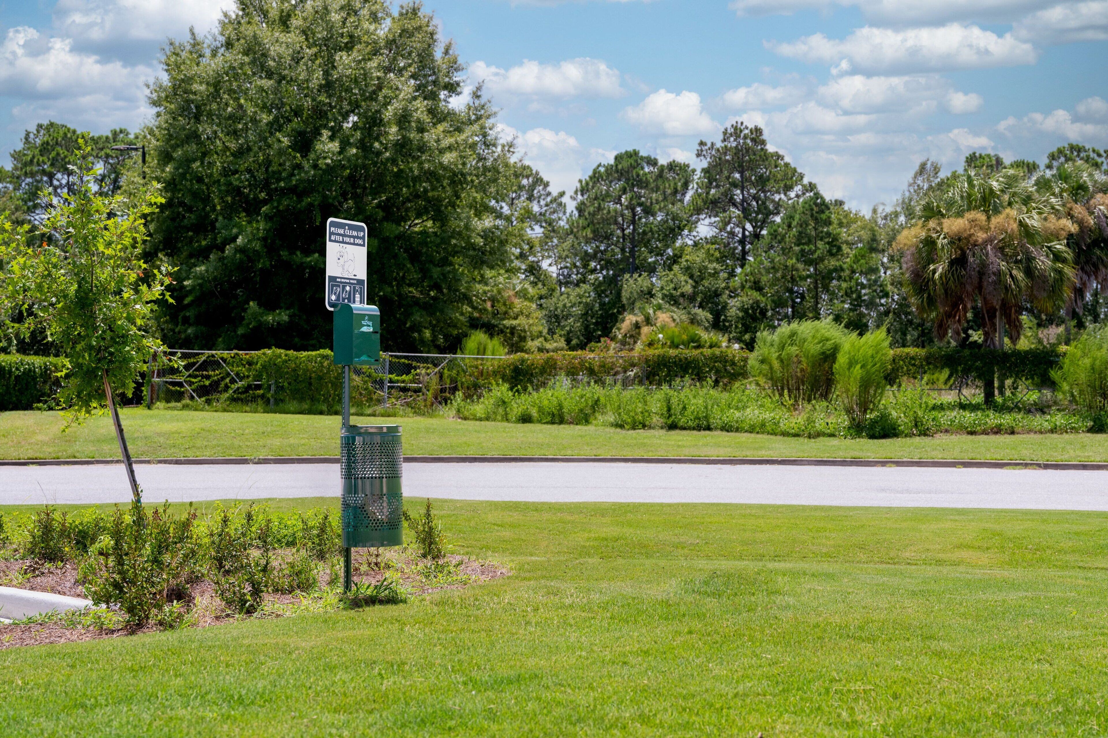 A green signpost with a map and directional information in a grassy area with trees and a road in the background.