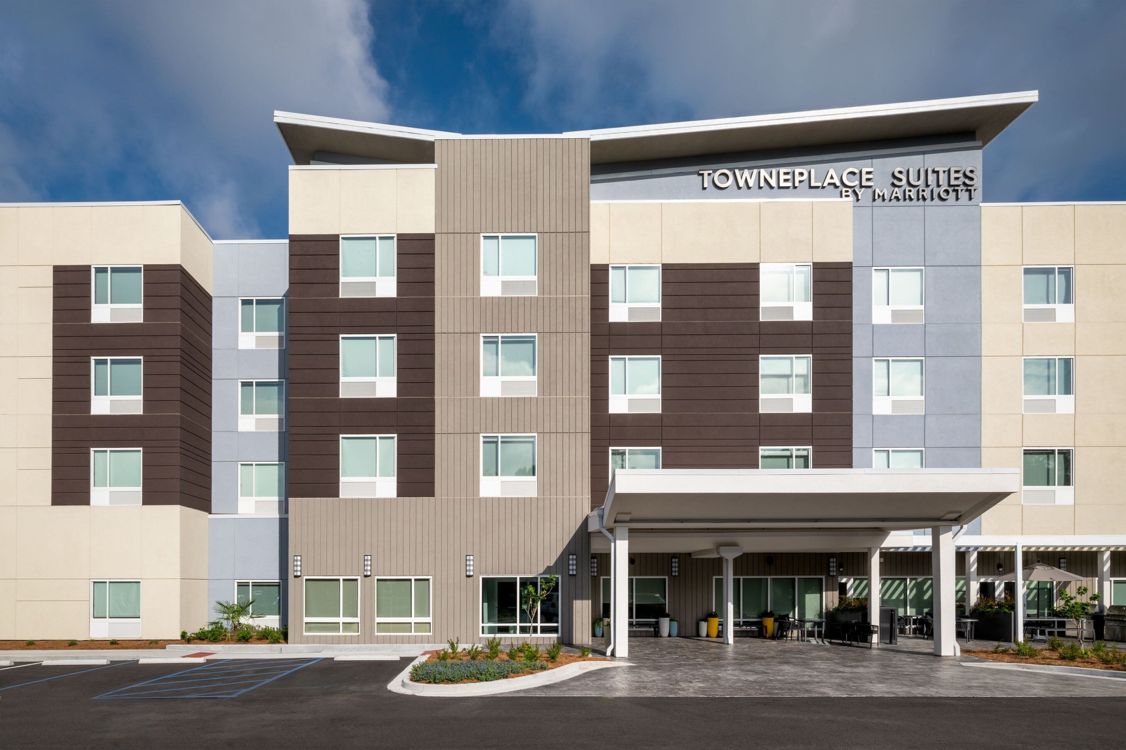 A multi-story hotel with a modern design, featuring a covered entrance area with outdoor seating and a parking lot.