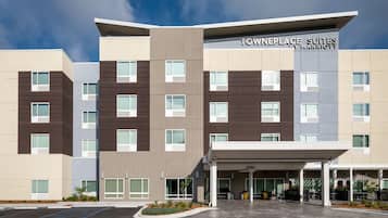 Een hotel met meerdere verdiepingen, met een modern design, voorzien van een overdekt entreegebied met zitplaatsen buiten en een parkeerplaats.