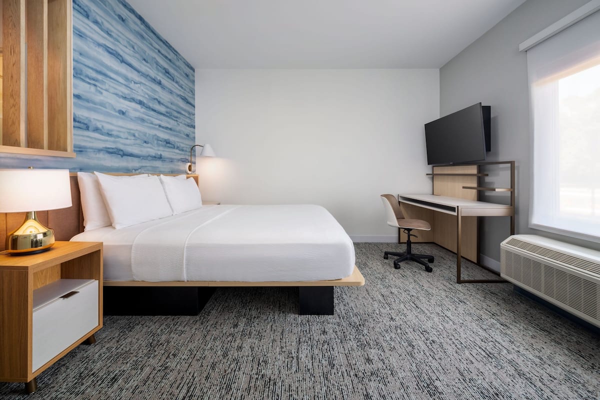 Ein Hotelzimmer mit Bett, Schreibtisch, Stuhl, Fernseher, Lampe und einem großen Fenster.
