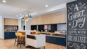 A modern kitchen with wooden cabinets, a central island with stools, and a chalkboard wall with a motivational message. - Towneplace Suites by Marriott Brunswick (Brunswick)